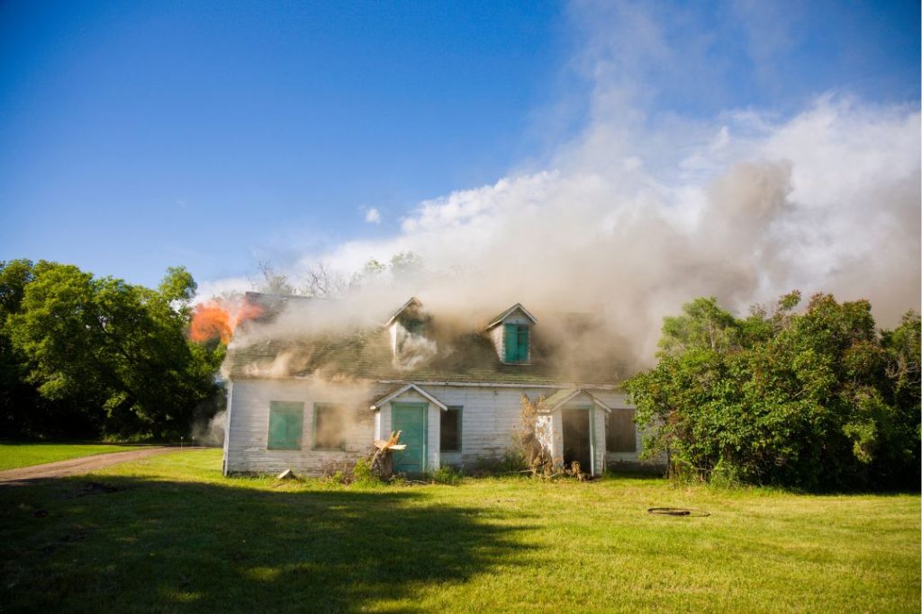 Vivienda afectada por un incendio con llamas visibles y humo saliendo por las ventanas.